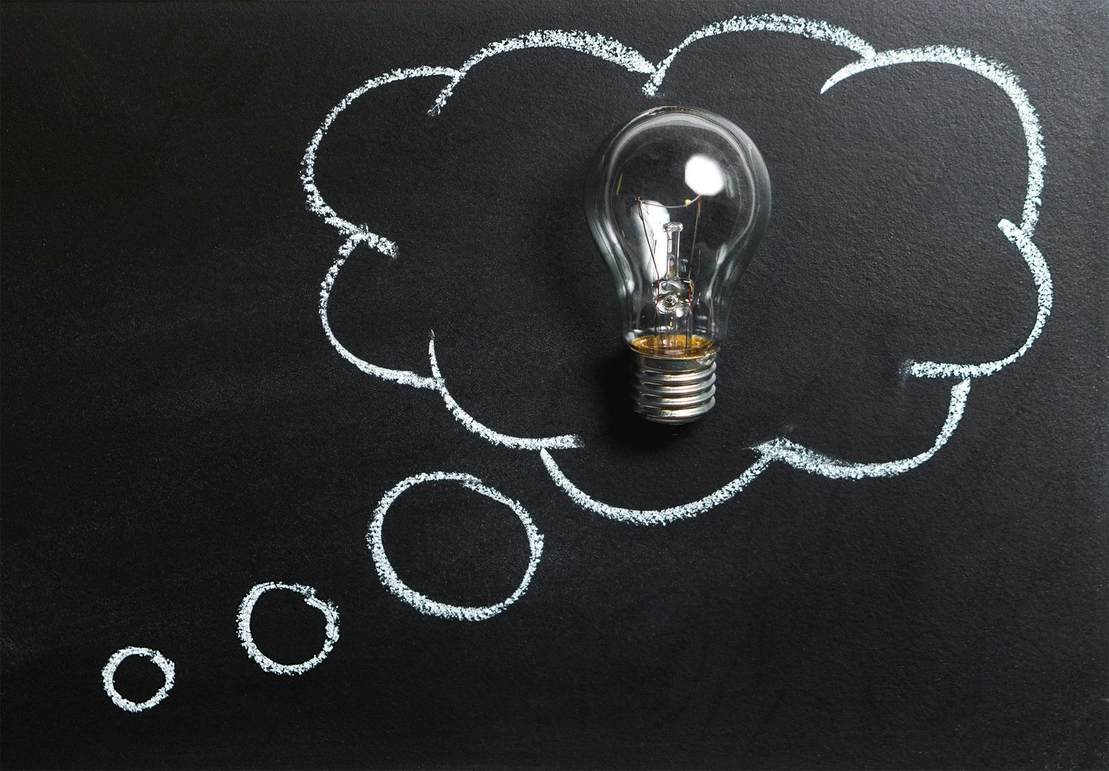 Home Light bulb laying on chalkboard with drawn thought bubble, symbolizing creative ideas.