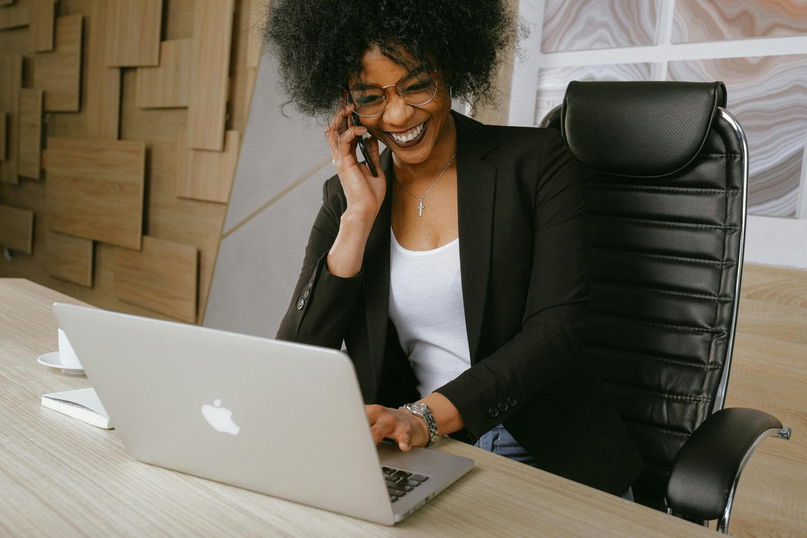 Home Smiling woman on phone call while working on a laptop in a stylish office.